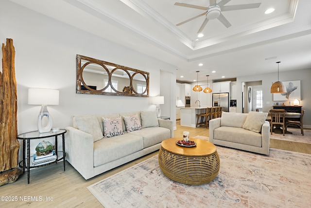 living area with crown molding, ceiling fan, light wood-type flooring, recessed lighting, and a raised ceiling