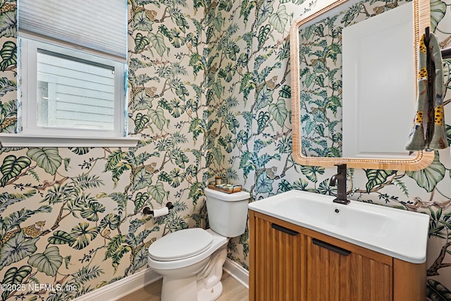 bathroom with toilet, wallpapered walls, vanity, and baseboards