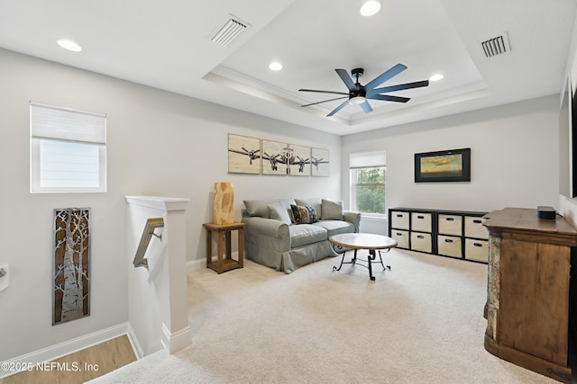 living area featuring a tray ceiling, visible vents, baseboards, and a ceiling fan