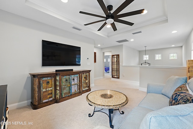 living room with baseboards, visible vents, ceiling fan, a raised ceiling, and light colored carpet