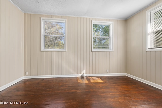 empty room with baseboards, a textured ceiling, dark wood finished floors, and crown molding