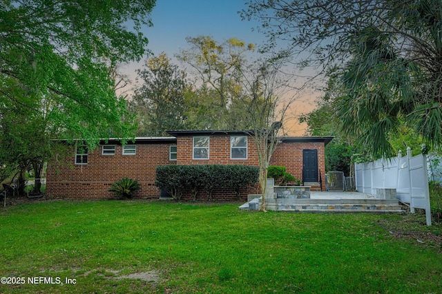 back of house at dusk featuring brick siding, a lawn, and fence