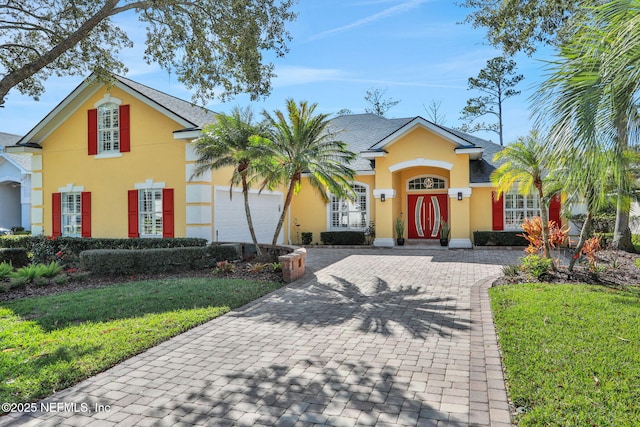 view of front of house with a front yard, decorative driveway, a garage, and stucco siding