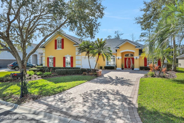 view of front facade with a front yard, decorative driveway, a garage, and stucco siding