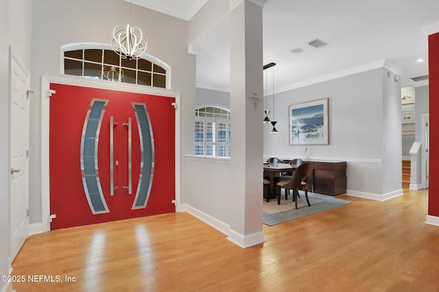 foyer entrance with visible vents, crown molding, baseboards, a chandelier, and wood finished floors