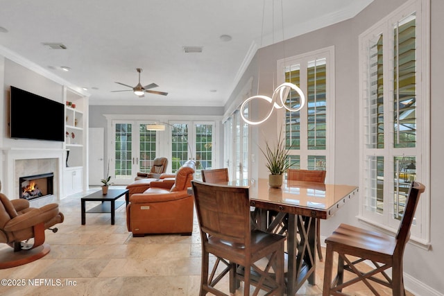 dining room featuring visible vents, a warm lit fireplace, and crown molding