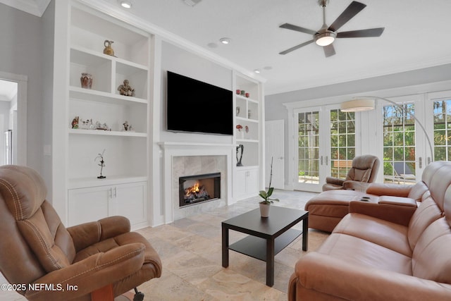 living room featuring built in shelves, a ceiling fan, ornamental molding, and a tiled fireplace