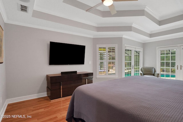 bedroom featuring access to exterior, visible vents, light wood finished floors, a tray ceiling, and french doors