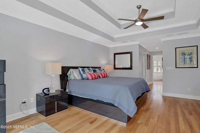 bedroom featuring a tray ceiling, baseboards, light wood-style flooring, and ornamental molding