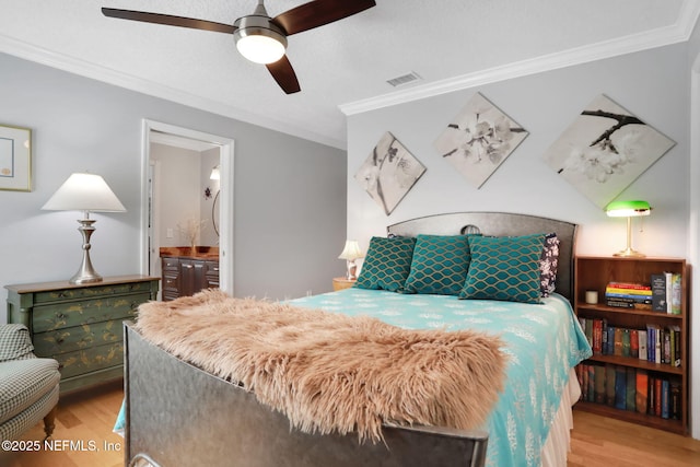 bedroom featuring ensuite bath, wood finished floors, visible vents, and ornamental molding