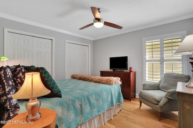 bedroom with two closets, light wood-type flooring, ceiling fan, and ornamental molding