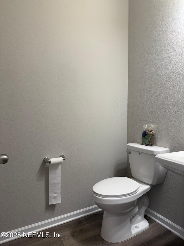 bathroom featuring baseboards, toilet, wood finished floors, and a textured wall