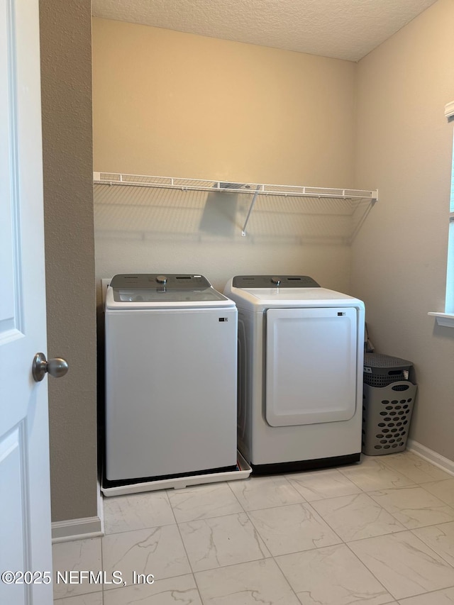 washroom featuring baseboards, washing machine and dryer, laundry area, marble finish floor, and a textured ceiling