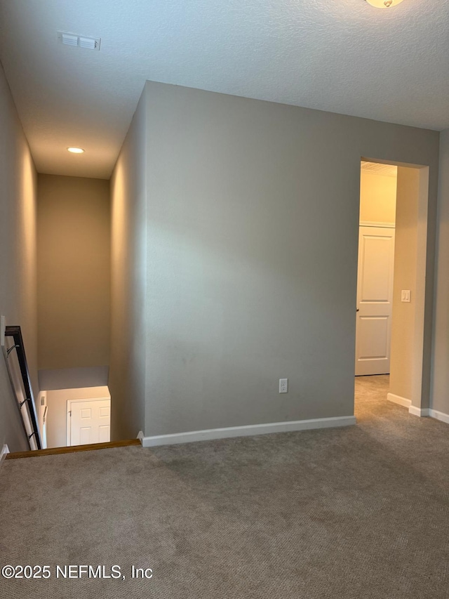 carpeted spare room featuring visible vents, a textured ceiling, and baseboards