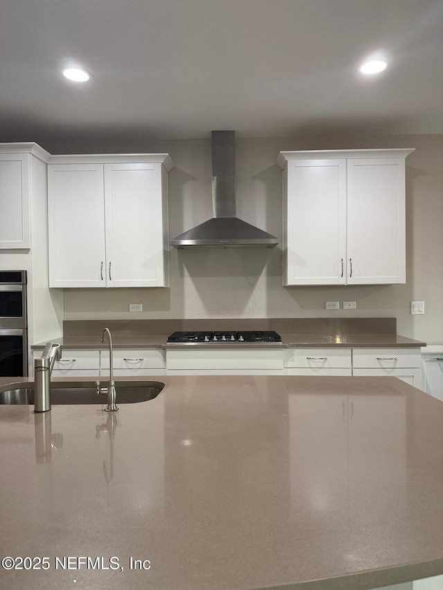 kitchen with a sink, white cabinetry, double oven, wall chimney exhaust hood, and black stovetop