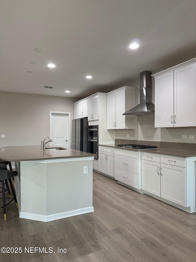 kitchen featuring gas cooktop, freestanding refrigerator, a sink, wall chimney exhaust hood, and multiple ovens