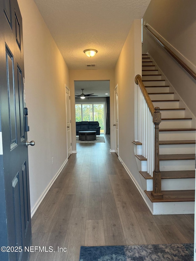 foyer entrance featuring dark wood-style floors, baseboards, visible vents, stairs, and a textured ceiling