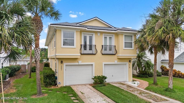 townhome / multi-family property with a front lawn, fence, stucco siding, a balcony, and a garage