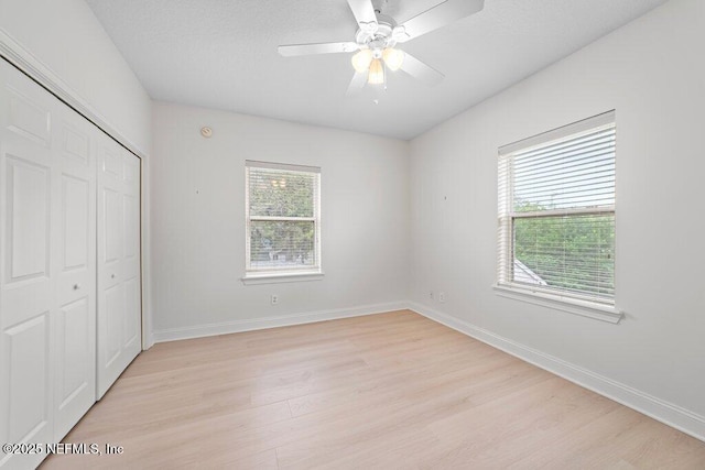 unfurnished bedroom featuring light wood finished floors, multiple windows, baseboards, and a closet