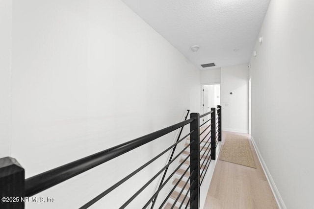 corridor featuring visible vents, an upstairs landing, a textured ceiling, light wood finished floors, and baseboards