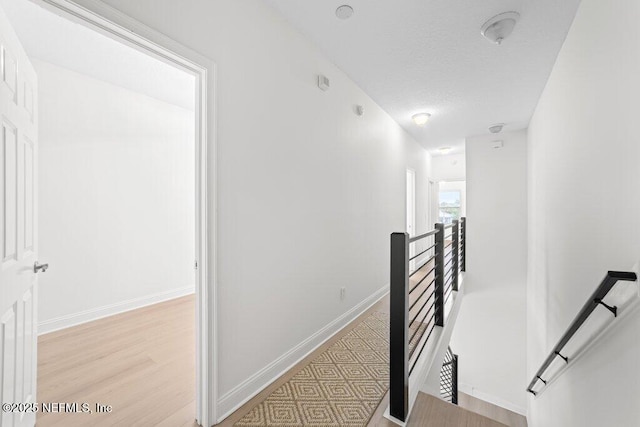 corridor with light wood-style floors, an upstairs landing, baseboards, and a textured ceiling