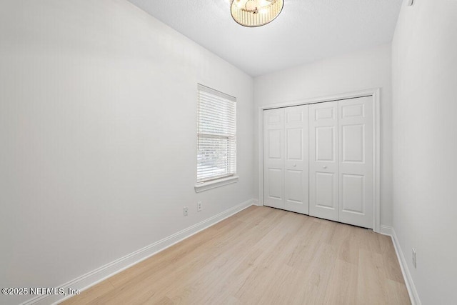 unfurnished bedroom featuring light wood-style floors, baseboards, and a closet