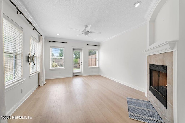 unfurnished living room with a tiled fireplace, light wood-style flooring, a textured ceiling, and crown molding