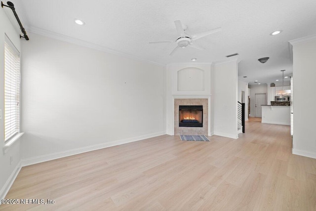 unfurnished living room featuring baseboards, light wood finished floors, ceiling fan, a tiled fireplace, and crown molding