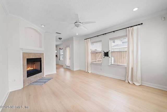 unfurnished living room with visible vents, ornamental molding, a textured ceiling, light wood-style floors, and a tile fireplace