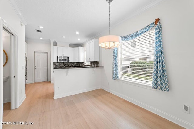 kitchen featuring ornamental molding, stainless steel microwave, backsplash, dark countertops, and white cabinets