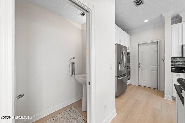 kitchen with visible vents, light wood-style flooring, tasteful backsplash, white cabinetry, and appliances with stainless steel finishes