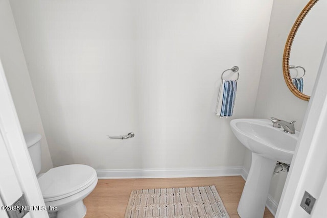 half bathroom featuring toilet, wood finished floors, baseboards, and a sink