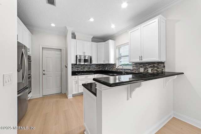 kitchen with visible vents, light wood finished floors, a breakfast bar, a peninsula, and stainless steel appliances