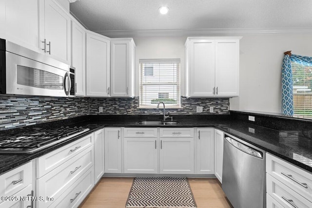 kitchen featuring light wood-style flooring, ornamental molding, a sink, white cabinets, and appliances with stainless steel finishes