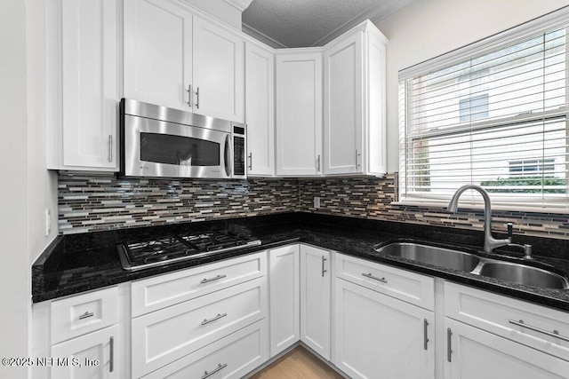 kitchen featuring a sink, stainless steel microwave, gas cooktop, tasteful backsplash, and white cabinetry