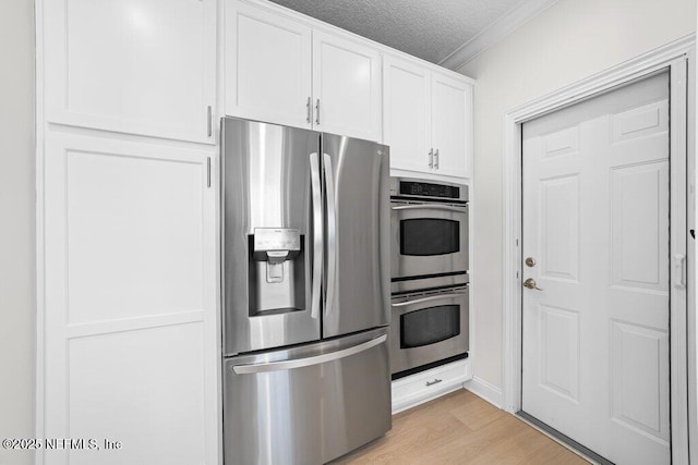 kitchen with light wood finished floors, ornamental molding, appliances with stainless steel finishes, a textured ceiling, and white cabinetry