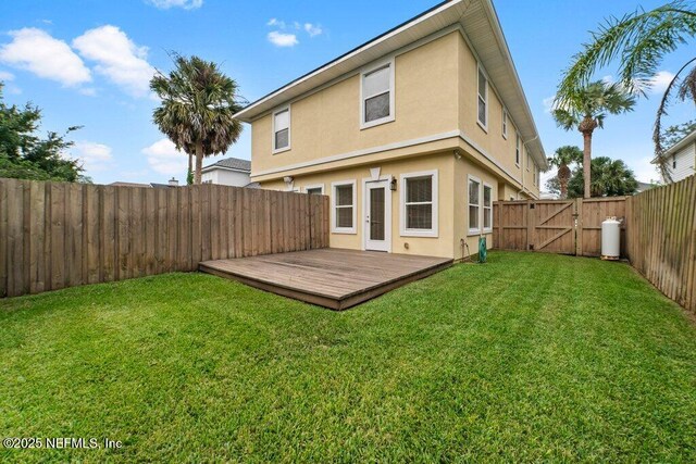 back of property featuring stucco siding, a yard, a deck, a fenced backyard, and a gate