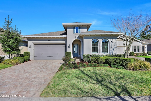 view of front facade with decorative driveway, a front yard, an attached garage, and stucco siding