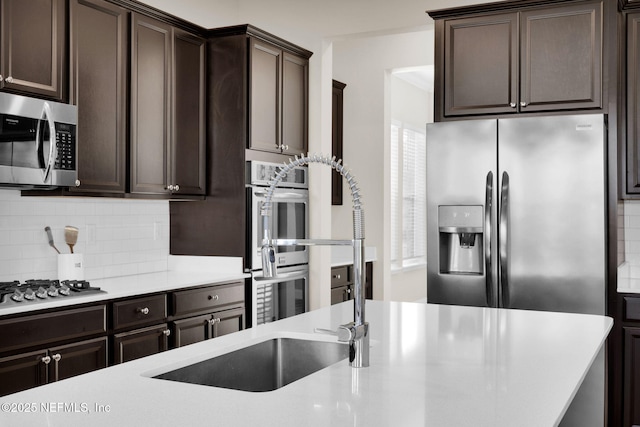 kitchen featuring tasteful backsplash, dark brown cabinetry, light countertops, appliances with stainless steel finishes, and a sink