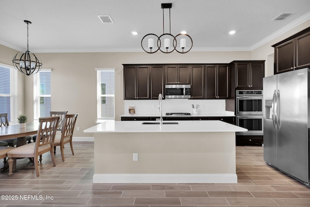 kitchen featuring wood finish floors, a sink, stainless steel appliances, a notable chandelier, and backsplash