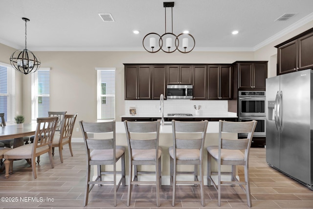 kitchen with visible vents, backsplash, appliances with stainless steel finishes, an inviting chandelier, and dark brown cabinets