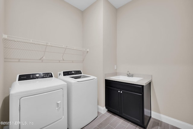 washroom with baseboards, wood tiled floor, cabinet space, a sink, and independent washer and dryer