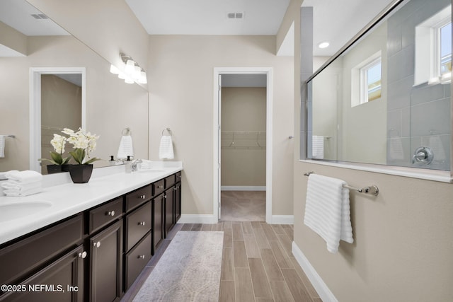 bathroom with a sink, tiled shower, double vanity, baseboards, and a spacious closet