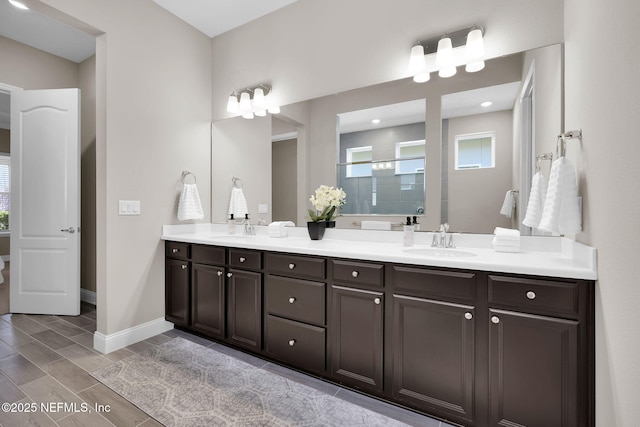 full bathroom with double vanity, baseboards, a tile shower, and a sink