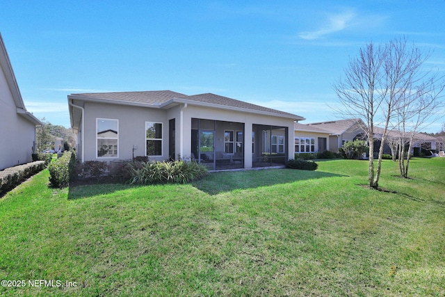 rear view of property with stucco siding, a yard, and a sunroom