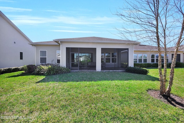 rear view of house with a lawn, a sunroom, and stucco siding