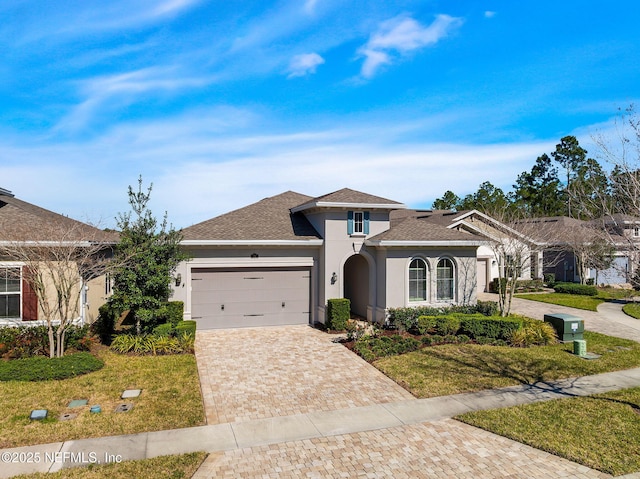 view of front of home featuring stucco siding, decorative driveway, a garage, and a front yard