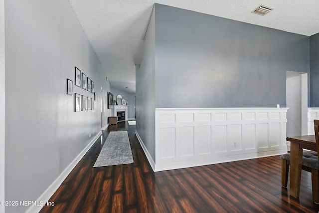 hall with visible vents, a textured ceiling, baseboards, and dark wood-style flooring