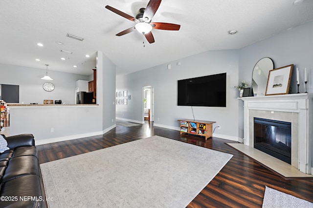 living area with visible vents, dark wood-style floors, a premium fireplace, baseboards, and vaulted ceiling