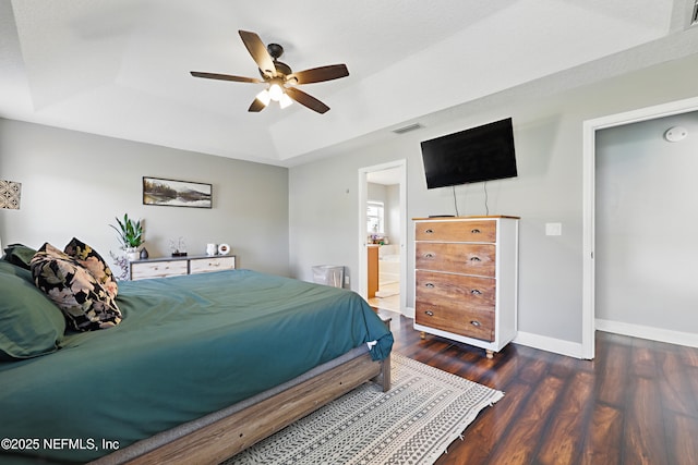 bedroom featuring visible vents, ensuite bath, wood finished floors, baseboards, and a raised ceiling